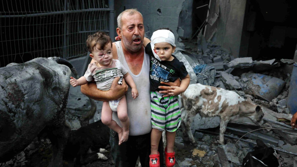 En palestinsk man bär sina skadade barnbarn efter bombningen av Nuseirat-lägret i Gaza, oktober 2023.